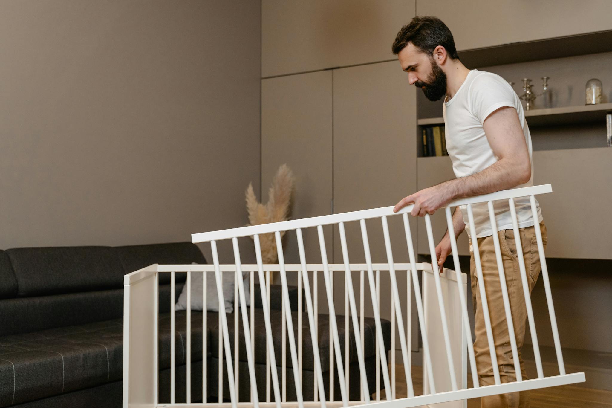 A bearded man assembles a crib in a stylish living room setting.