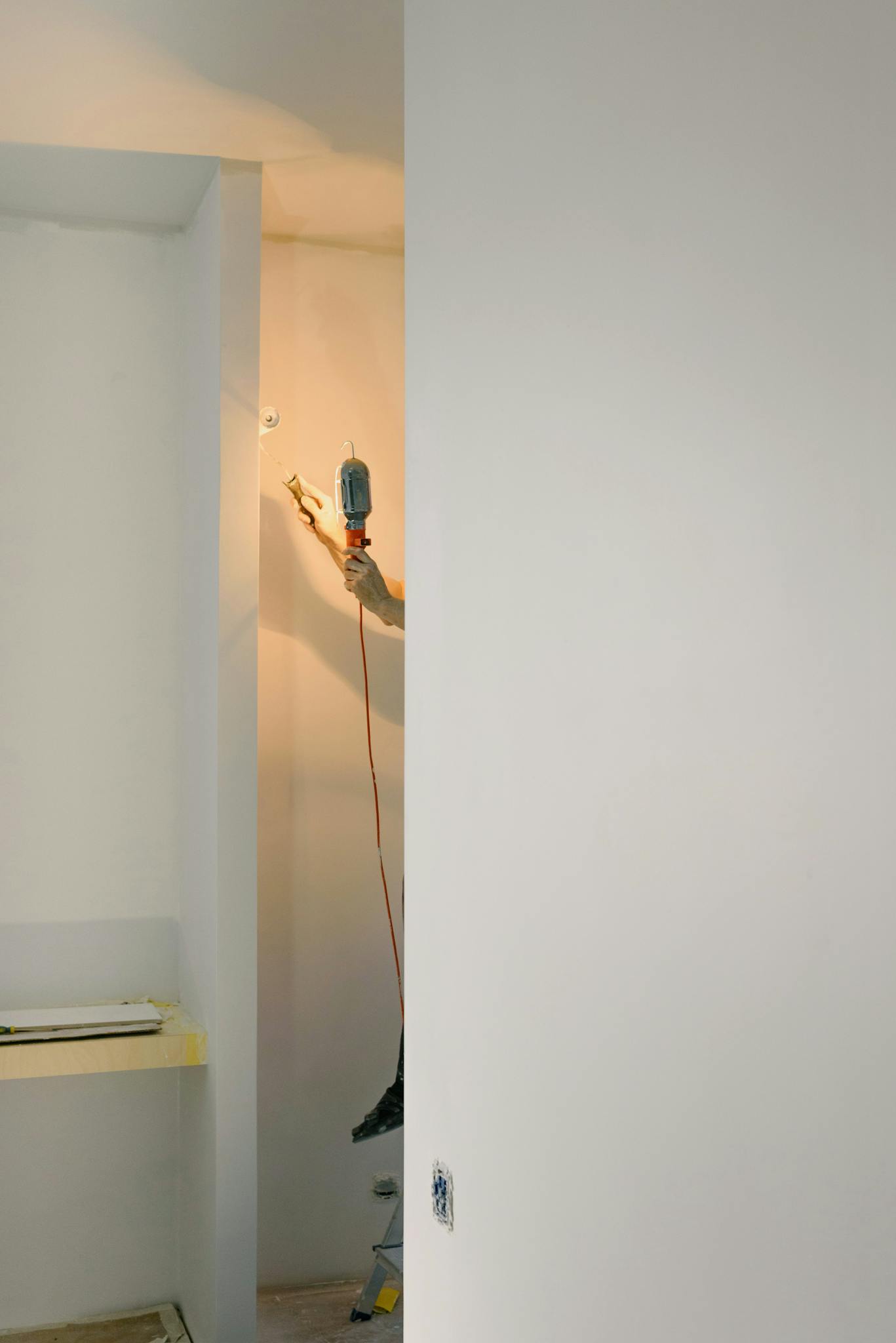 Crop faceless handyman standing on ladder while holding lamp and working in room